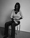 Die Atempädagogin Claudia Kaltenbach sitzt auf einem Hocker und zeigt die Körperübung „Oberschenkel klopfen“.